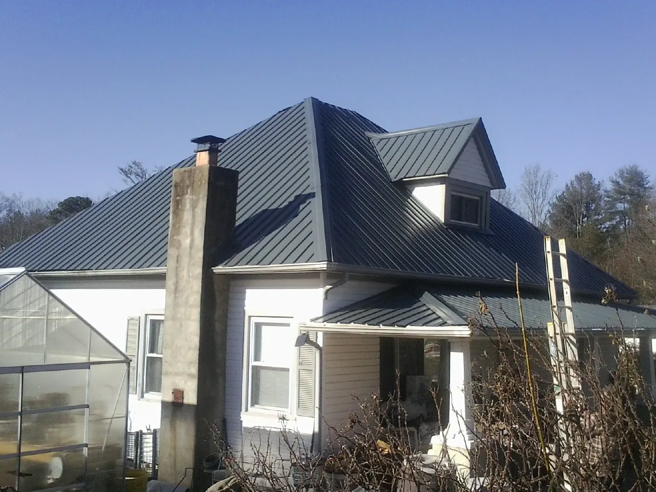 Dark blue standing seam metal roof on a white farmhouse with dormer — Slate & Tile Roof Repair by Roofing Brothers in Niles