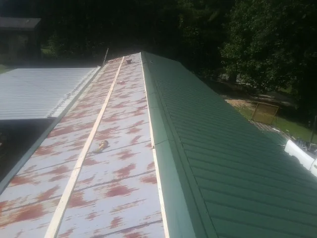 Old rusted panels beside newly installed green metal roofing — Wind Damage Roof Repair by Roofing Brothers in Niles