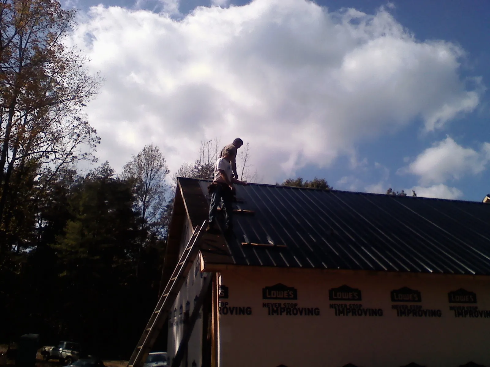 Roofer fastening dark metal panels high against a cloudy sky, from a Roof Inspection job in Niles